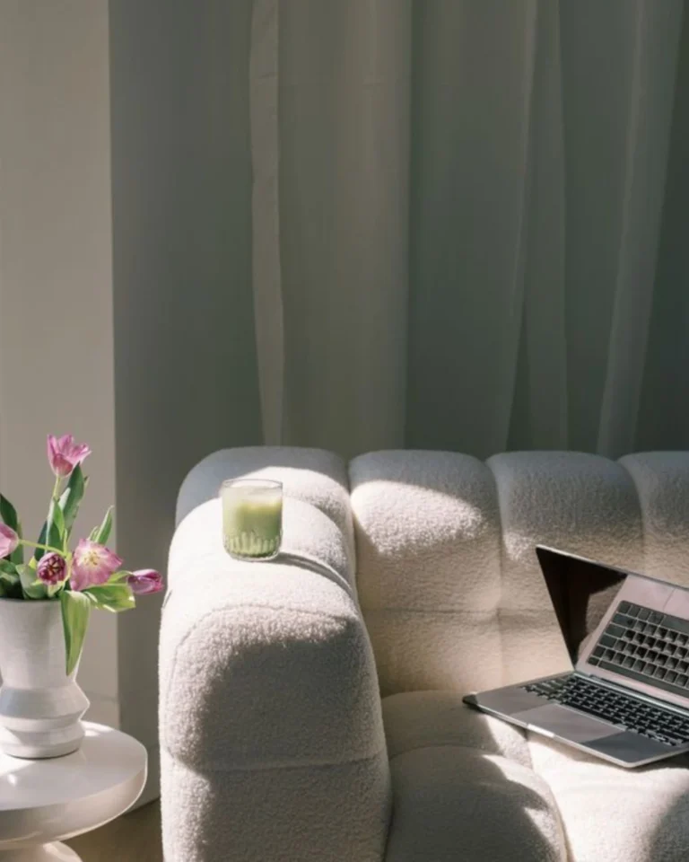 MacBook on a white couch with pink flowers in a vase on a side table